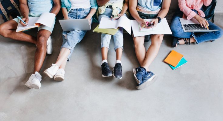 overhead portrait young people with laptops smartphones sitting together floor students writing lectures holding textbooks their knees