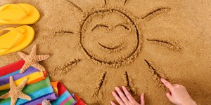 Child drawing a smiling sun on a sandy beach, with beach towel, starfish and flip flops (studio shot - warm color and directional light are intentional).