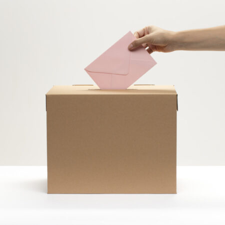 hand puts pink envelope into vote box